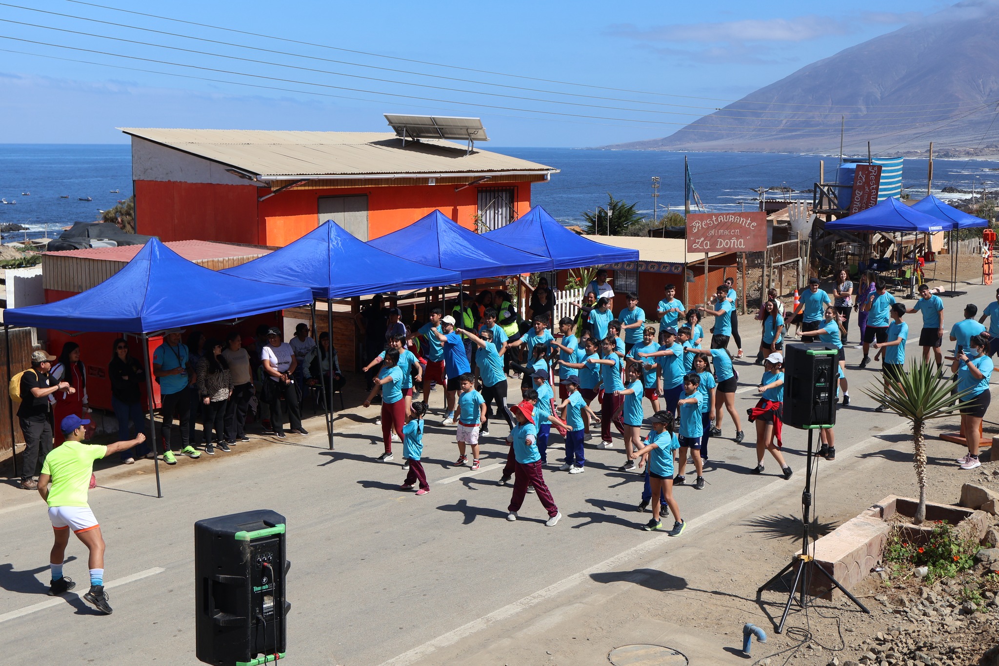 Vecinas y vecinos participan en la activación física y baile inicial de la Corrida Familiar de Paposo 2025, con vista al mar y organización municipal.