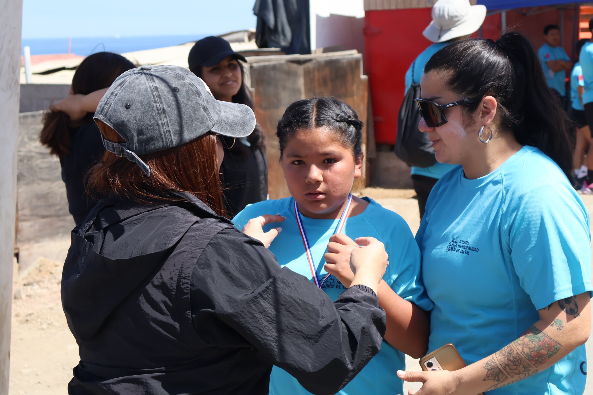 Funcionarias municipales entregan medalla a participante infantil tras completar la Corrida Familiar de Paposo 2025 en la localidad costera.