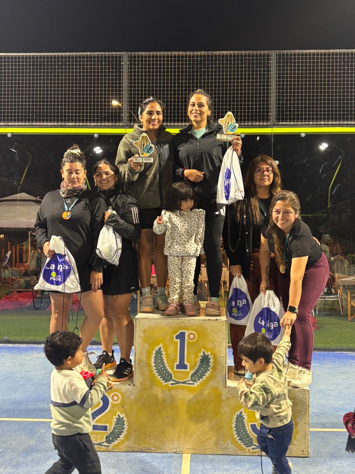Campeonas y finalistas de la categoría C damas posando en el podio junto a sus hijos durante la premiación de La Liga Caleta Hueso Pádel 2025.