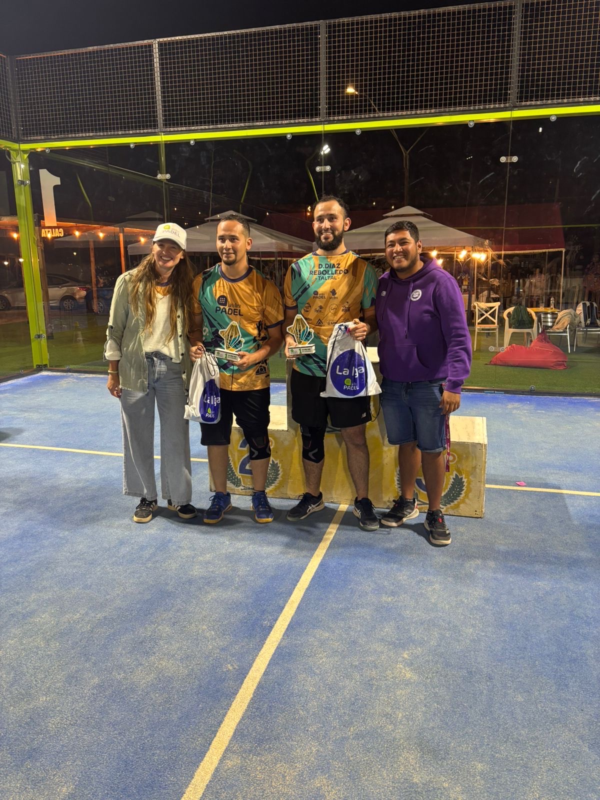 Dupla campeona de 5ta categoría varones posando con sus trofeos en el podio de La Liga Caleta Hueso Pádel 2025 en Taltal, acompañados por la organización del torneo.