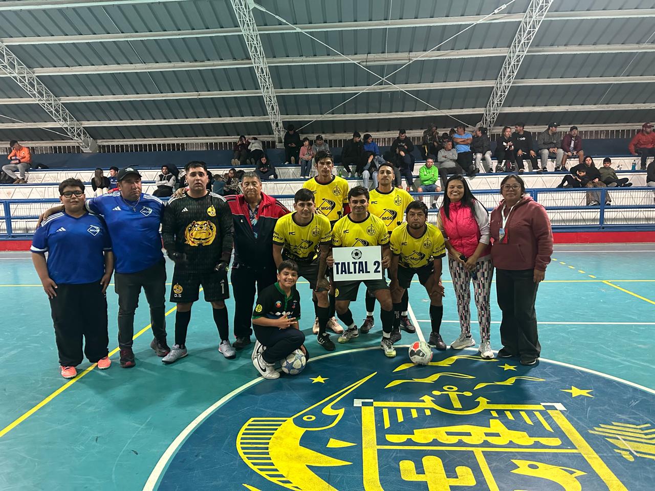 Equipo “Taltal 2”, de camiseta amarilla, posa en el centro del Estadio Techado antes de su compromiso inaugural.