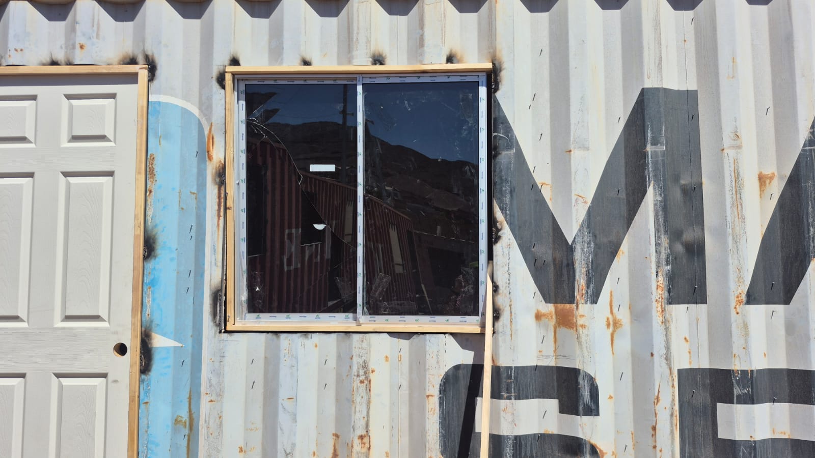 Vista cercana de un contenedor Maersk con una ventana de doble panel con vidrios rotos y marco de madera.