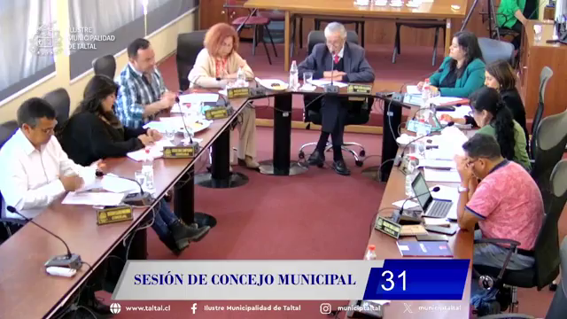 Concejales de Taltal en sesión ordinaria; dos ediles conversan frente a micrófonos en sala municipal de madera