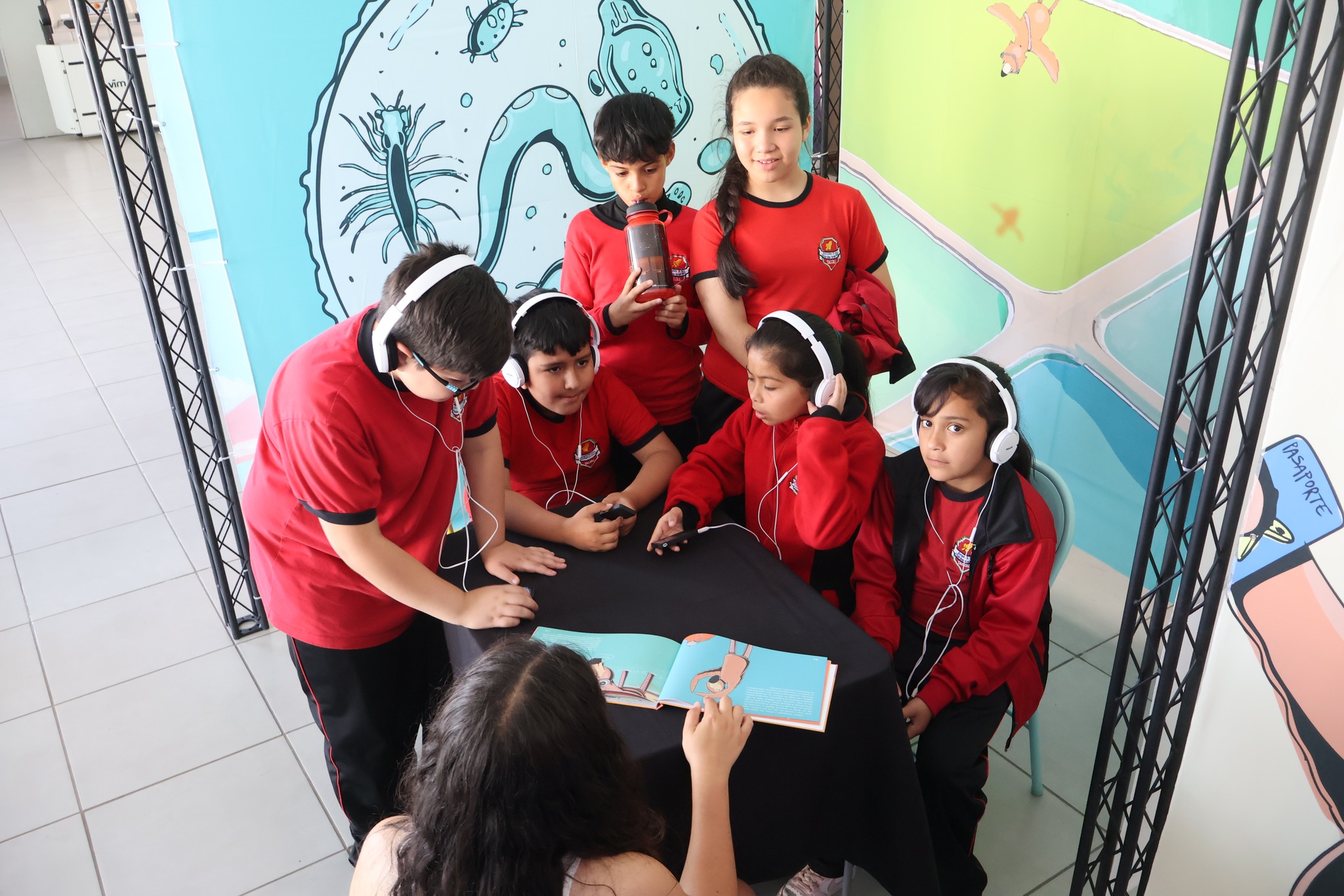Estudiantes con audífonos escuchan el cuento Tataira mientras revisan el libro ilustrado del proyecto educativo.