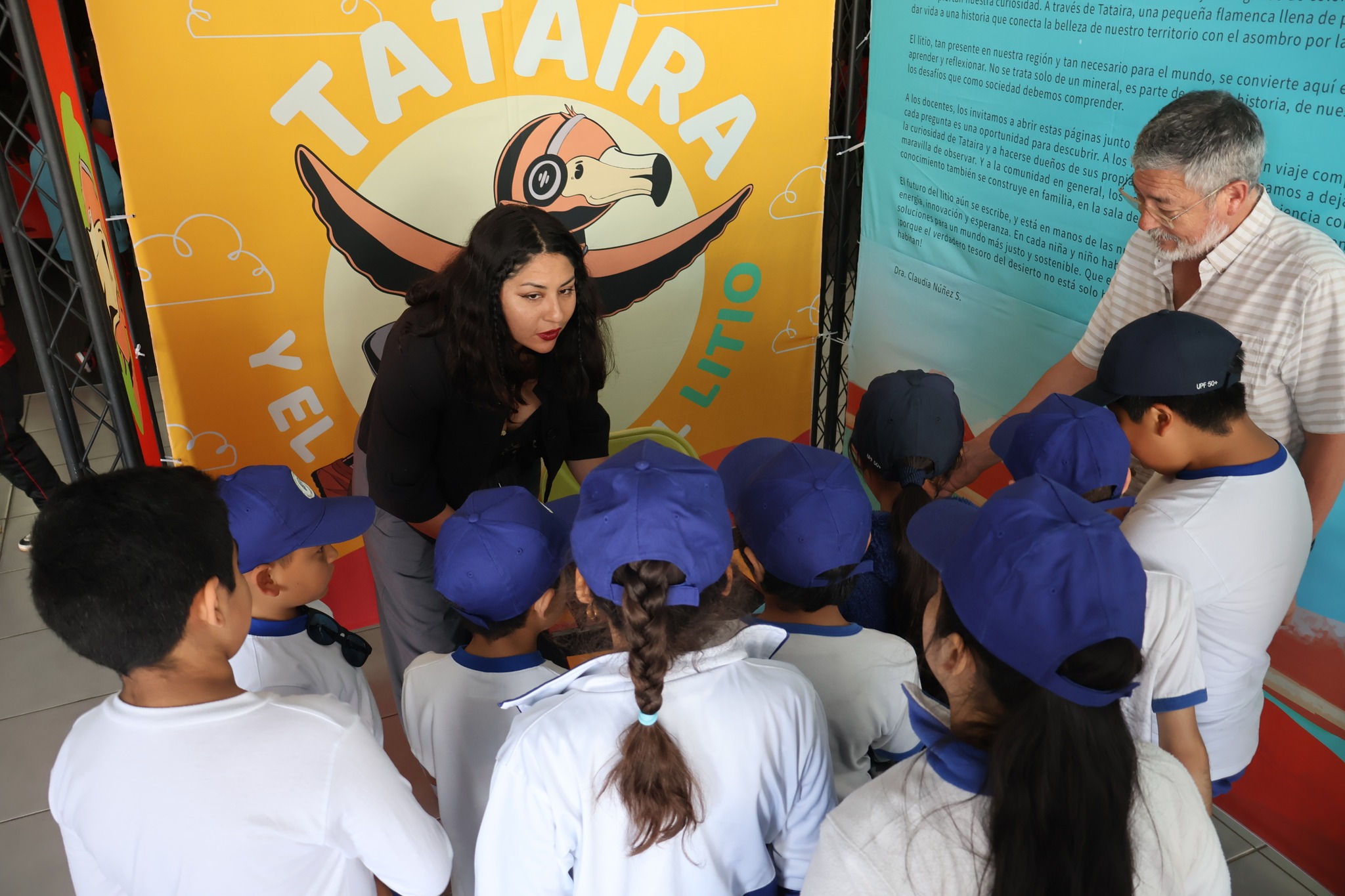 Facilitadora y académico explican contenidos del cuento Tataira a un grupo de estudiantes reunidos frente al módulo informativo.