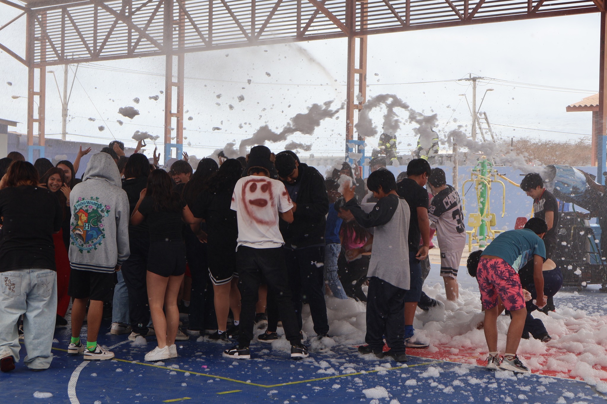 Estudiantes del Liceo Politécnico José Miguel Quiroz disfrutando de actividad recreativa con espuma en la cancha techada.