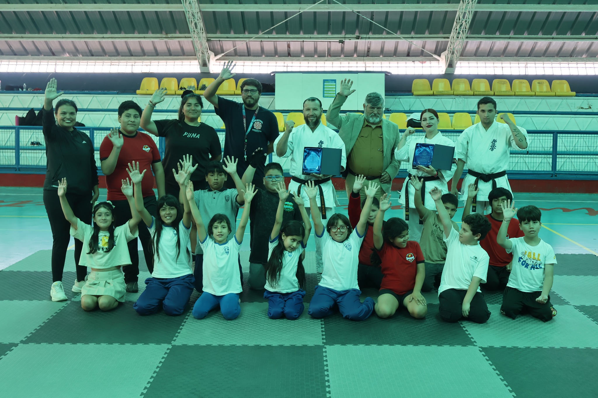 Foto grupal de niños y niñas de Taltal junto al campeón mundial Víctor Collao, la vicecampeona mundial Amei Collao, instructores y autoridades municipales tras la clase masiva de karate Kyokushin en el Estadio Techado de Taltal.