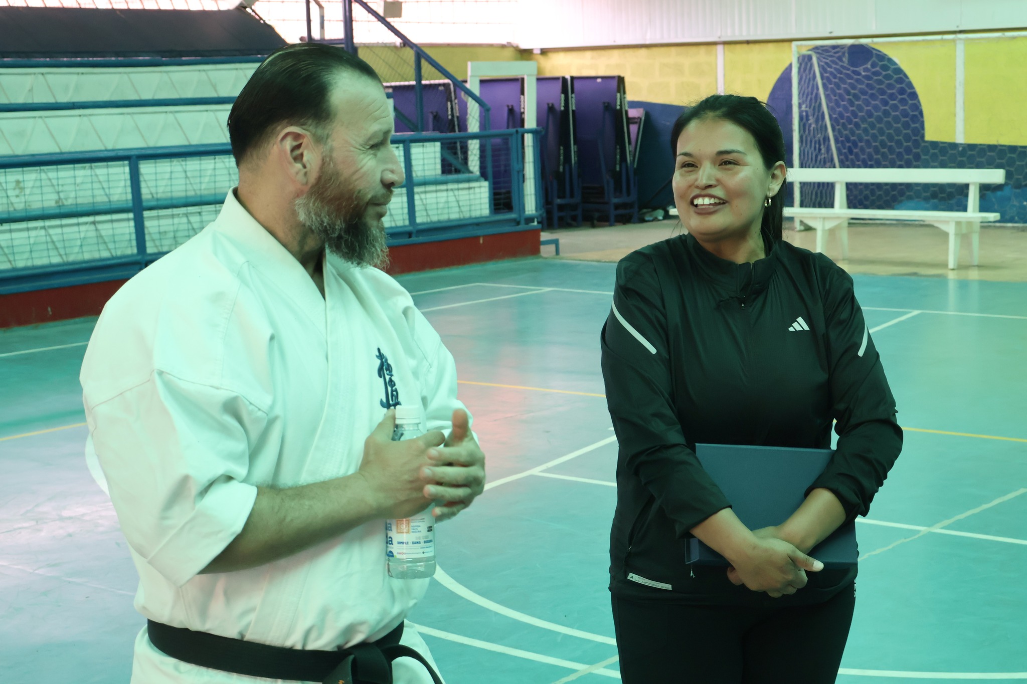 El campeón mundial de karate Víctor Collao conversa sonriente con la encarga de deporte y cultura del municipio Caren Huentupil en el Estadio Techado Municipal durante la jornada deportiva con estudiantes.
