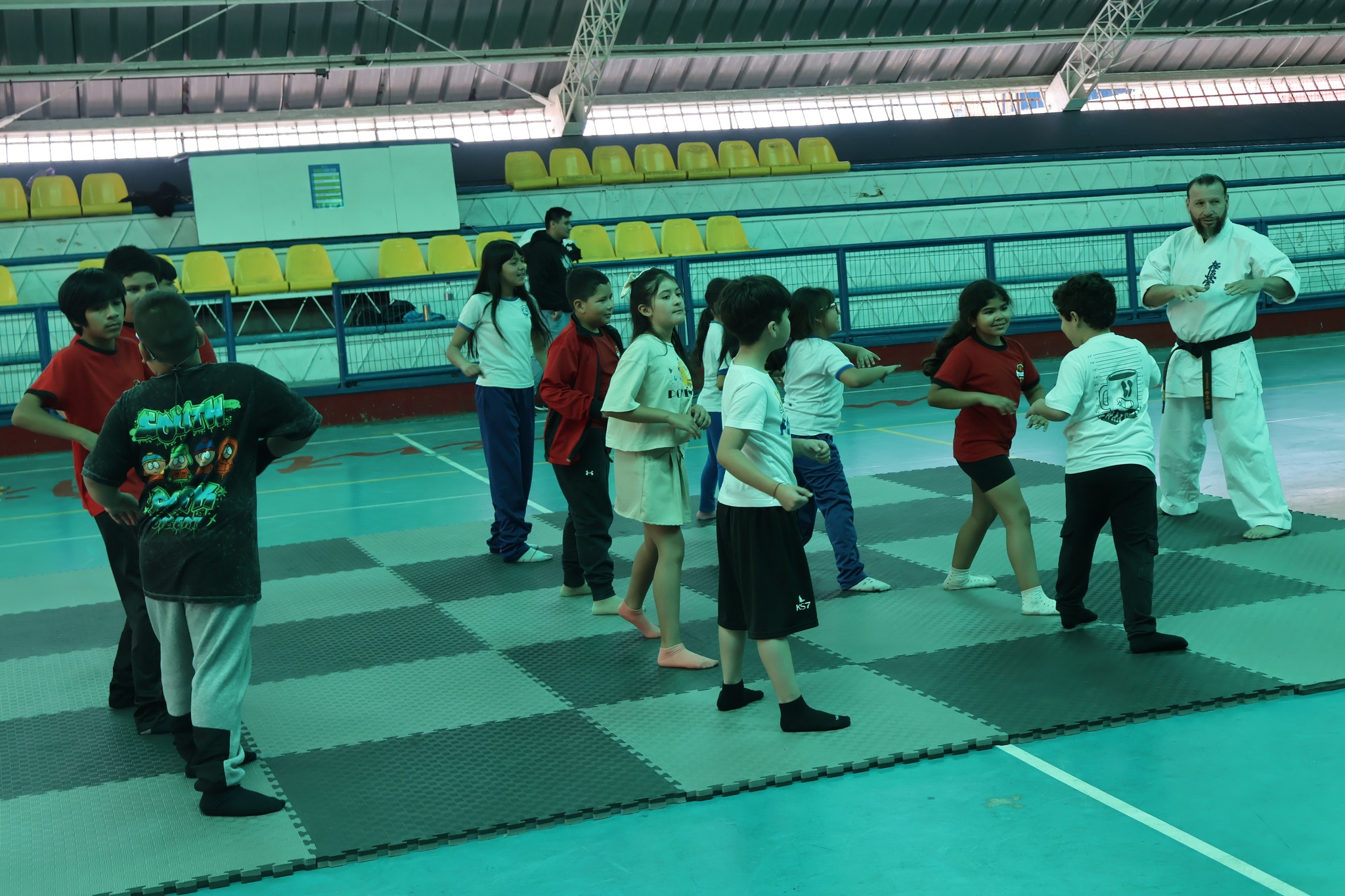 Niños y niñas corren y realizan ejercicios de coordinación sobre el tatami como parte del calentamiento guiado por los instructores de karate Kyokushin.