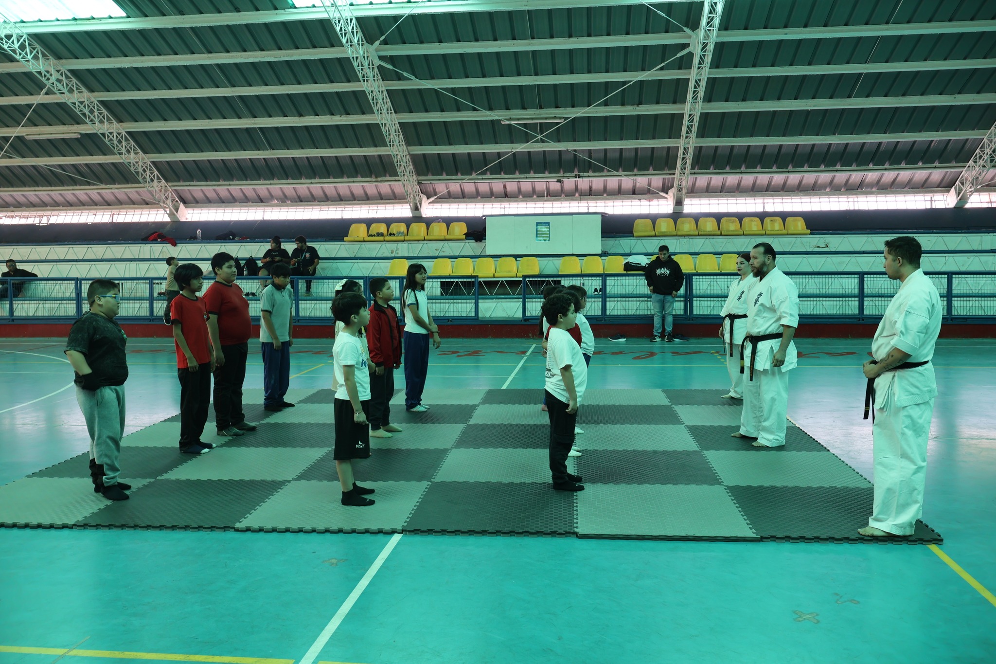 Niños y niñas del taller participan en la formación inicial del entrenamiento de karate Kyokushin junto a los instructores en el Estadio Techado Municipal.