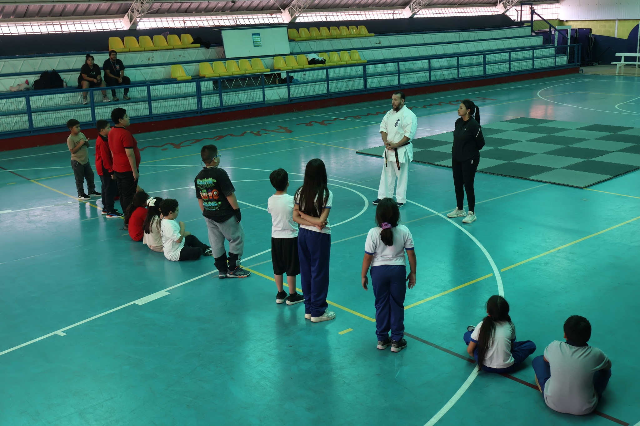 El sensei Víctor Collao conversa con estudiantes que escuchan atentamente durante la jornada deportiva en el Estadio Techado de Taltal.