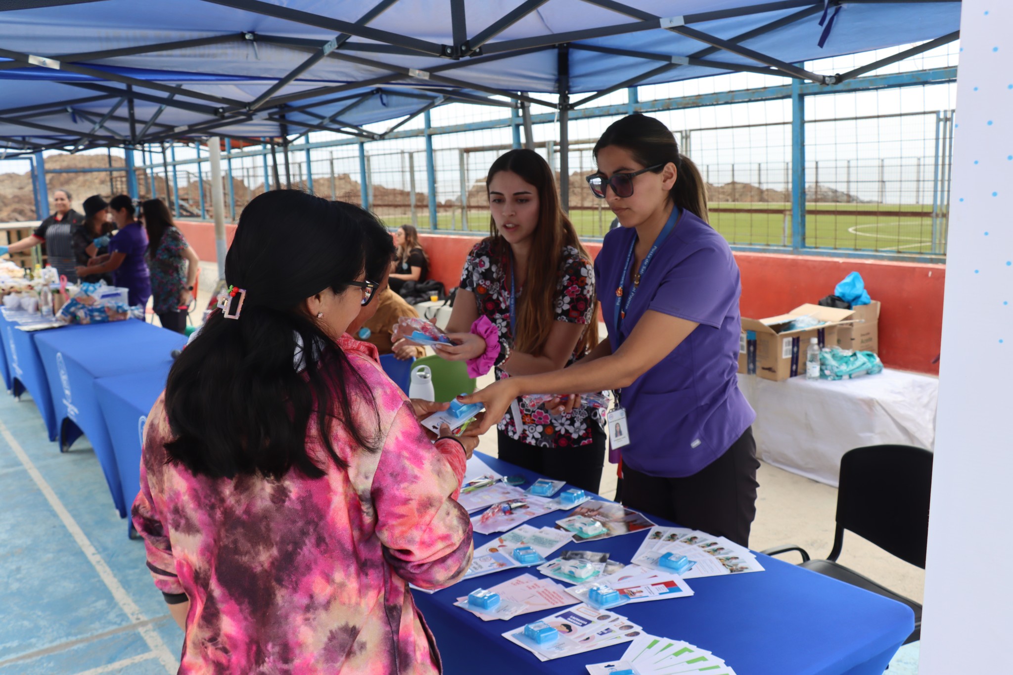 Funcionarias de salud entregando kits de autocuidado a vecinas en stand informativo.