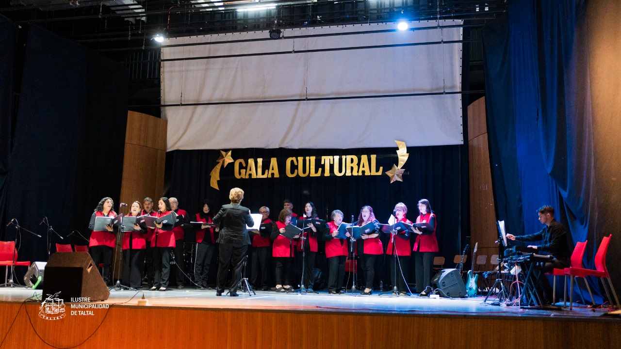 Coro de cámara con chalecos rojos siendo dirigido en el escenario de la Gala Cultural.