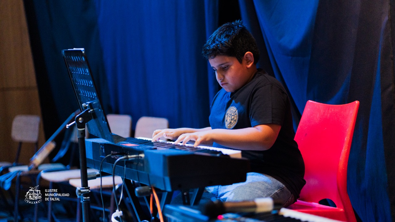 Primer plano de un niño estudiante concentrado tocando un teclado o piano electrónico en el escenario.