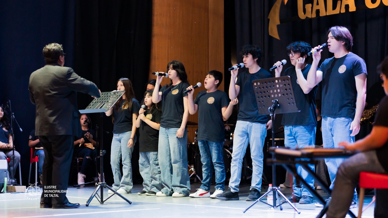 Grupo de jóvenes cantantes del Taller de Canto, con poleras negras, interpretando una pieza dirigidos por un monitor.