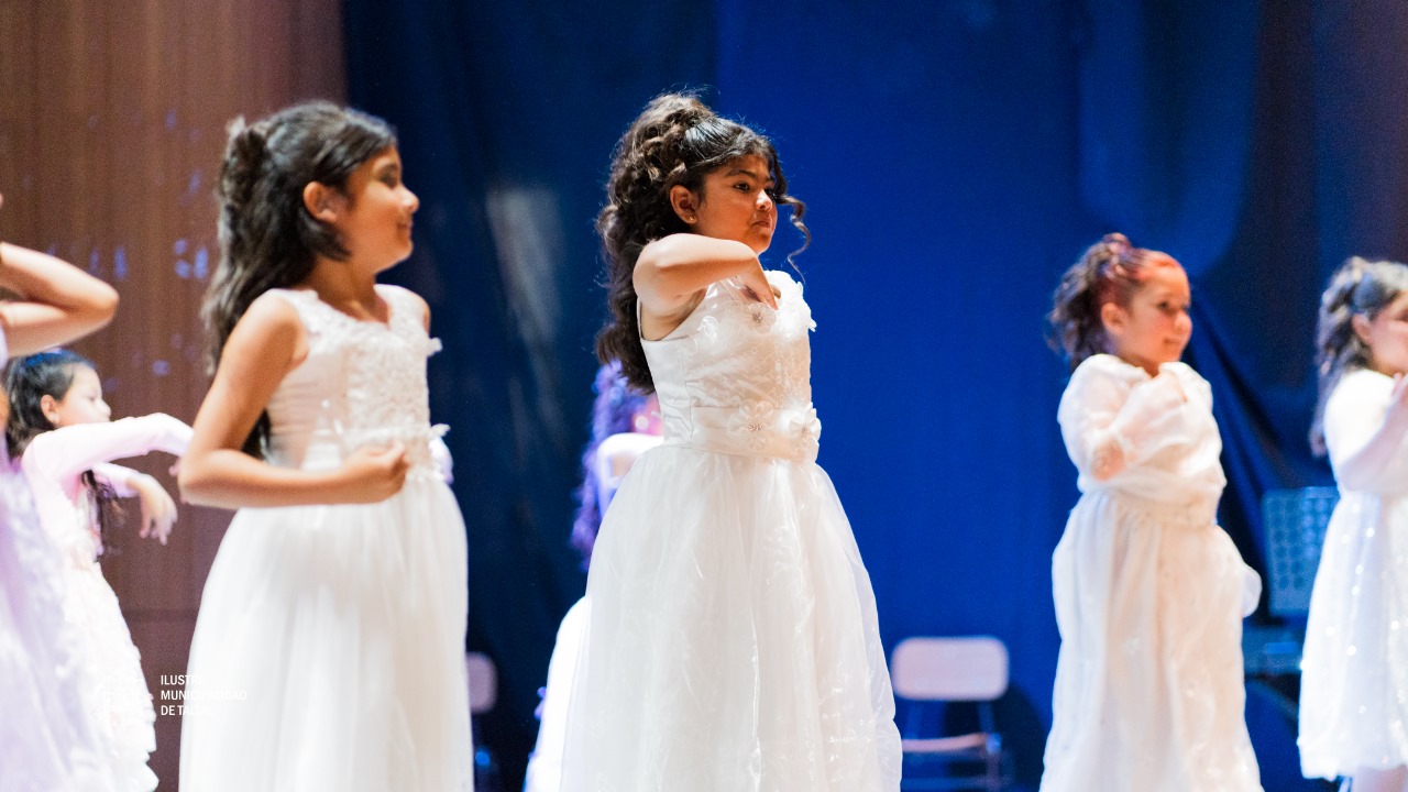 Primer plano de niñas del Taller de Danza en vestidos blancos, realizando movimientos en el escenario.