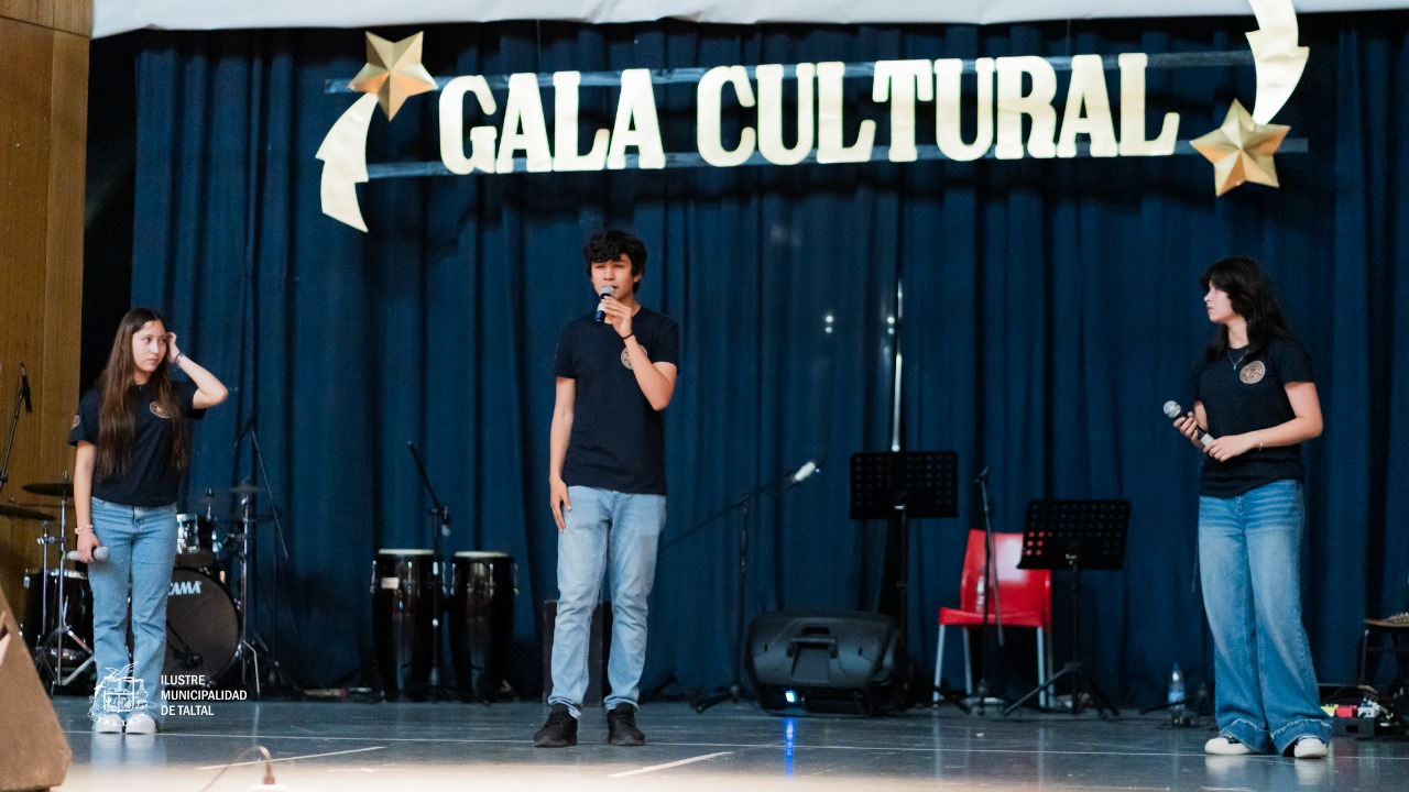 Tres jóvenes (dos mujeres y un hombre) de pie con micrófonos, posiblemente presentando una cancion