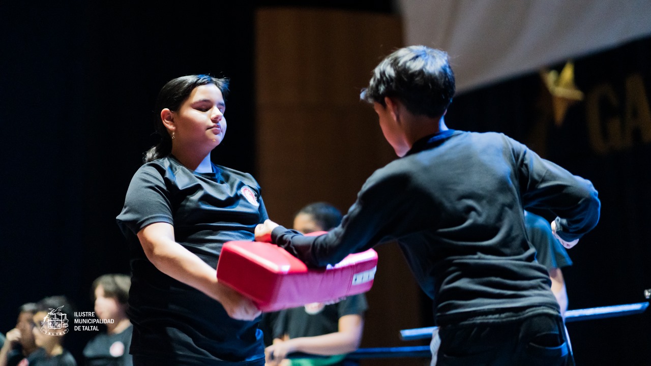 Niños de la Academia de Artes Marciales practicando un ejercicio de defensa personal o golpe sobre un cojín de impacto.