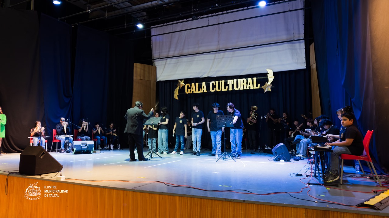 Gran ensamble instrumental de estudiantes siendo dirigido por un monitor en el centro del escenario.