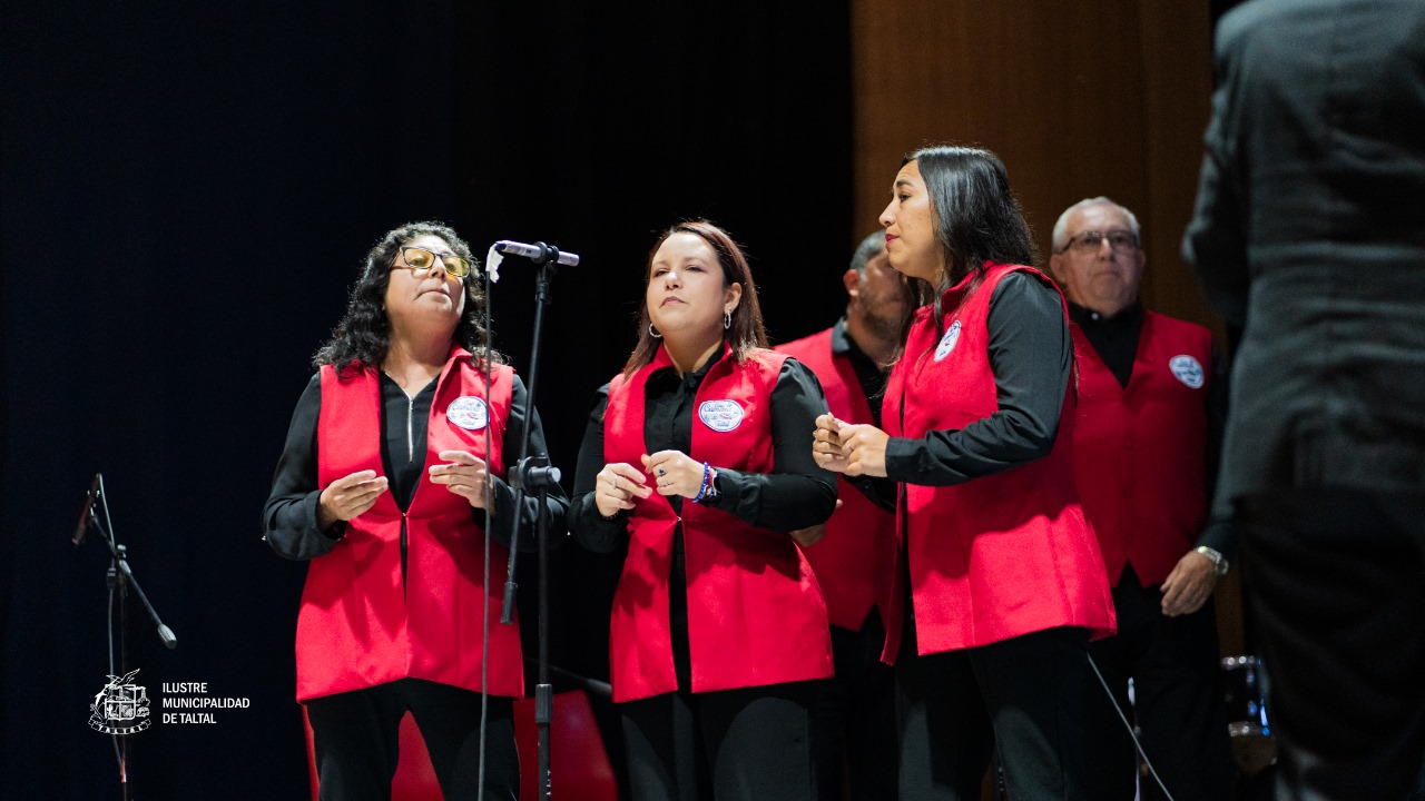 Primer plano de tres mujeres del coro con chalecos rojos cantando juntas.
