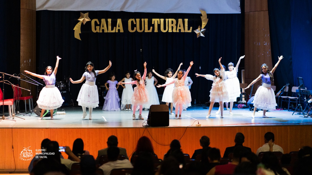 Coreografía final de las niñas del Taller de Danza con vestidos de tonos pasteles y blancos, levantando los brazos.