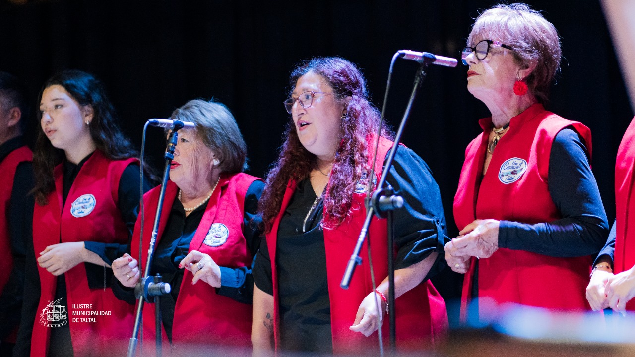 Mujeres del Coro de Cámara de Taltal cantando con chalecos rojos y micrófonos, mostrando un primer plano vocal.