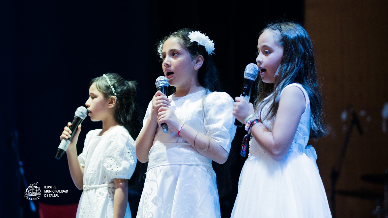Primer plano de tres niñas cantantes del Taller de Canto con vestidos blancos y flores en el cabello.