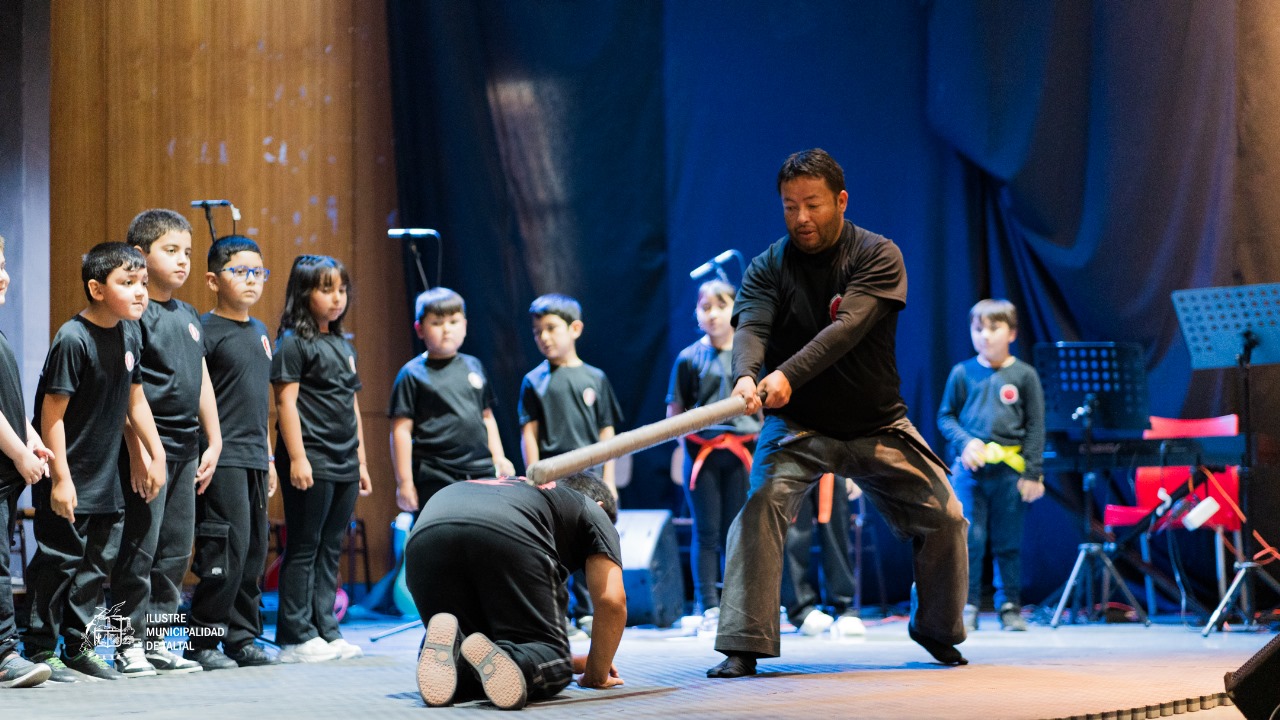 Monitor de la Academia de Artes Marciales realizando una demostración de fuerza sobre un alumno arrodillado.