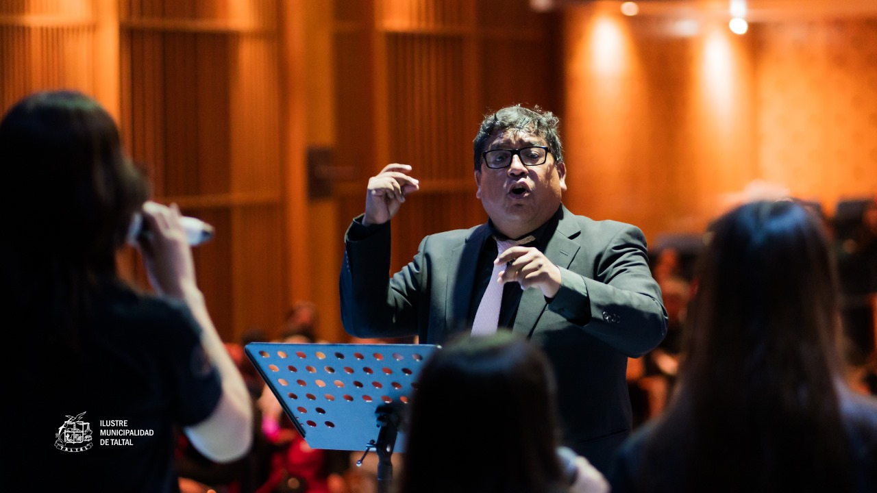 Director musical Sadrac Araya en traje gesticulando mientras dirige a un grupo de cantantes en el escenario.