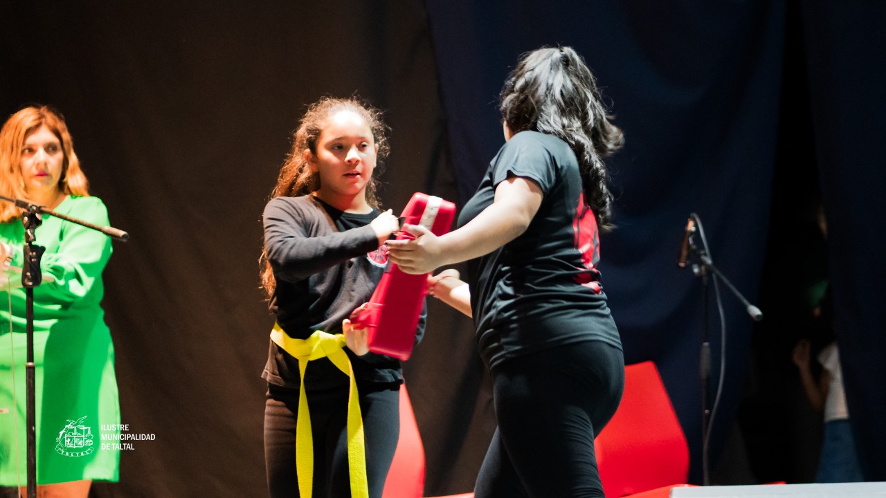 Alumna de artes marciales con cinturón amarillo recibiendo el impacto de un golpe en un cojín rojo.