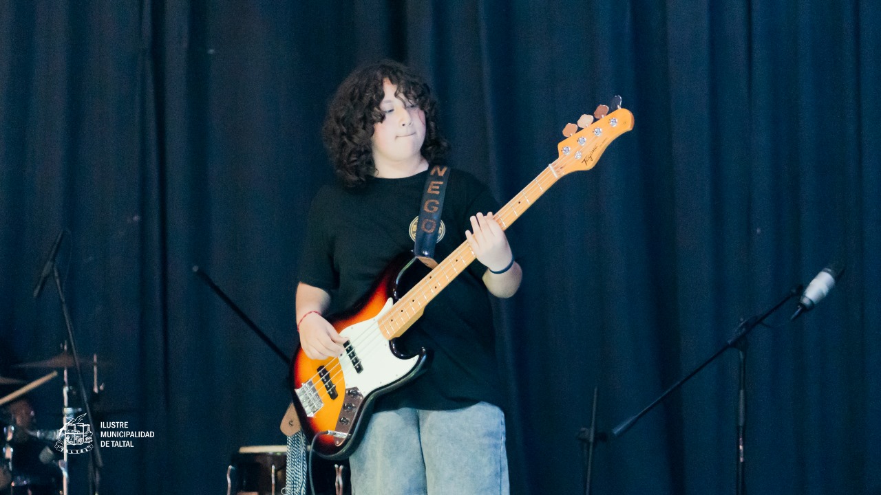 Primer plano de un joven músico concentrado tocando un bajo eléctrico.
