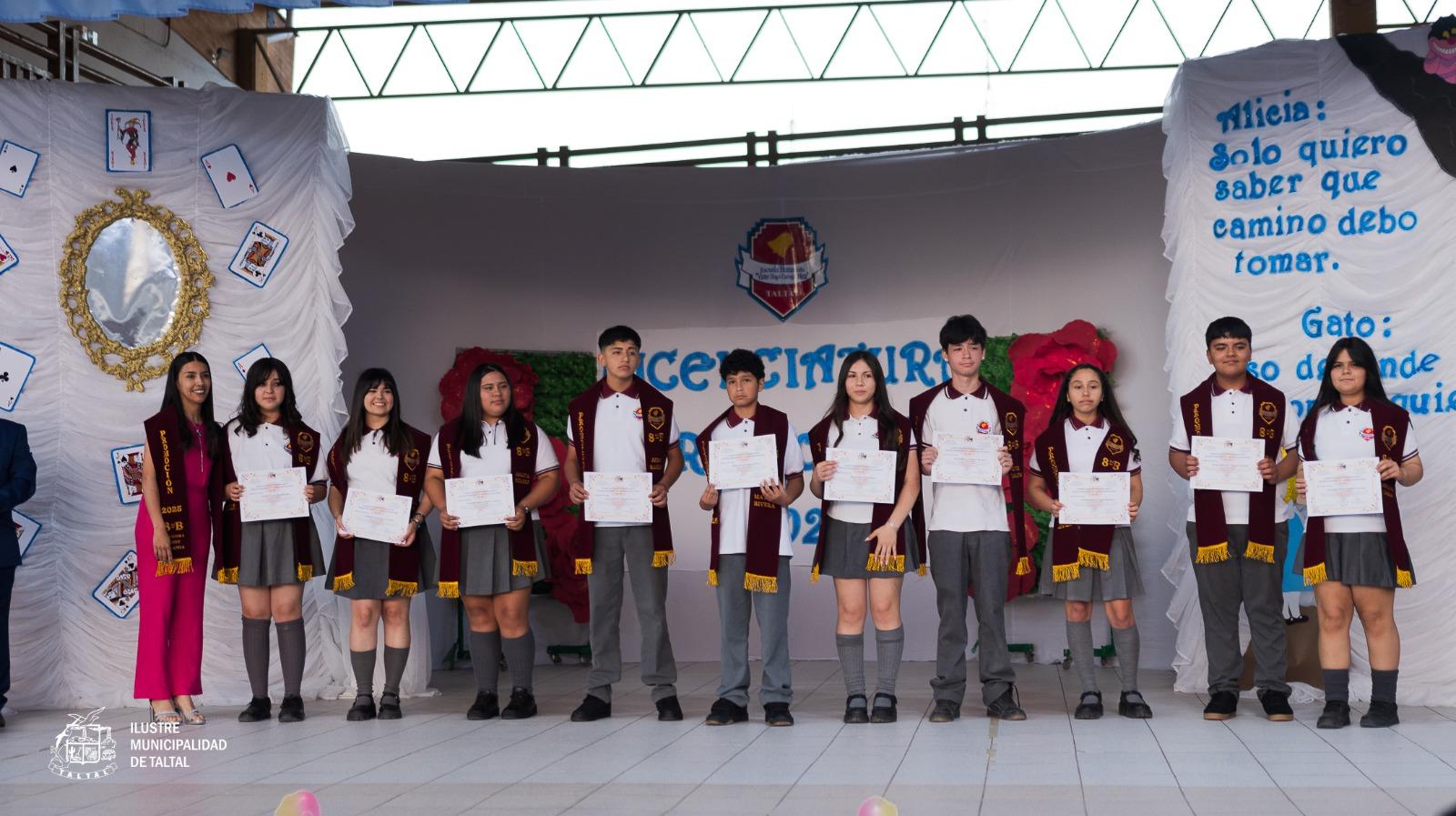 Grupo numeroso de estudiantes licenciados posando con sus diplomas en el escenario decorado.