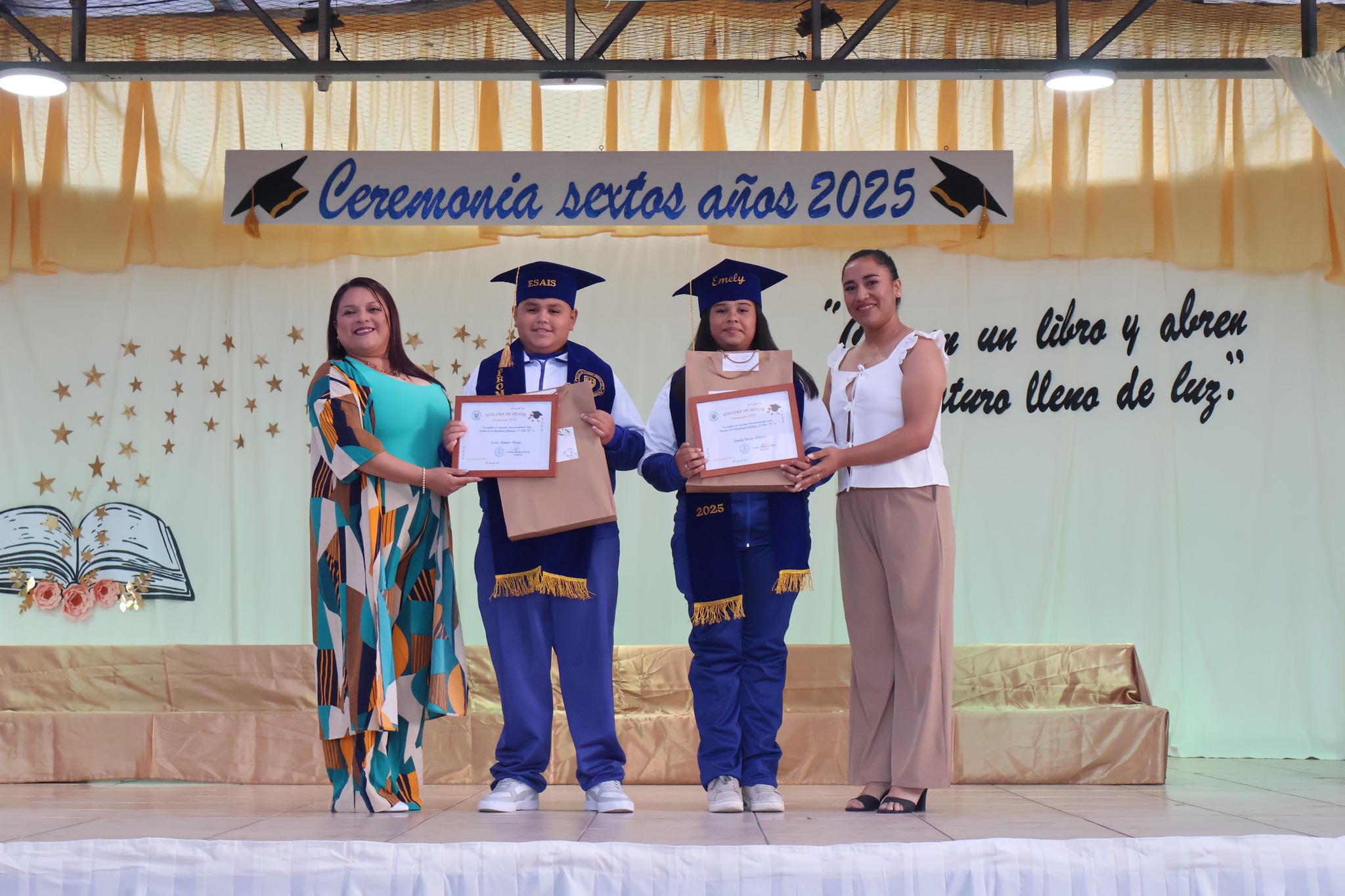 Dos estudiantes reciben distinción y posan con profesoras en ceremonia 2025.