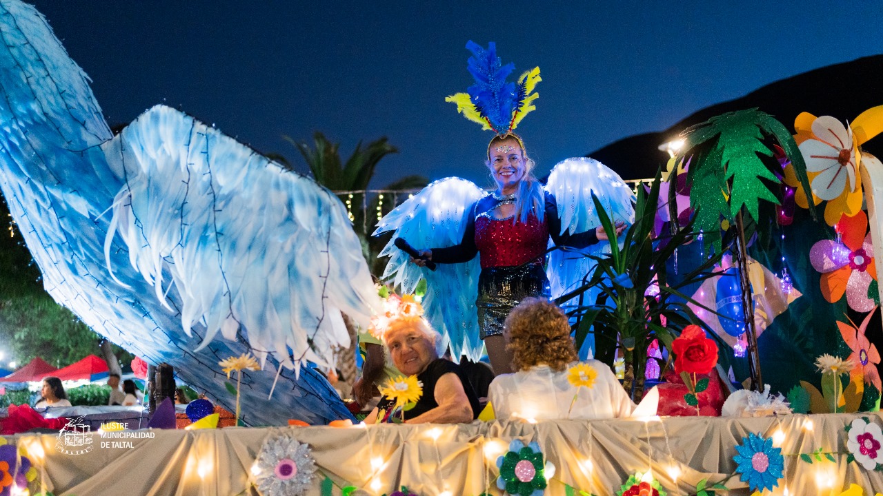 Artista sobre carro alegórico con grandes alas azules iluminadas durante la Caravana Navideña en Taltal.