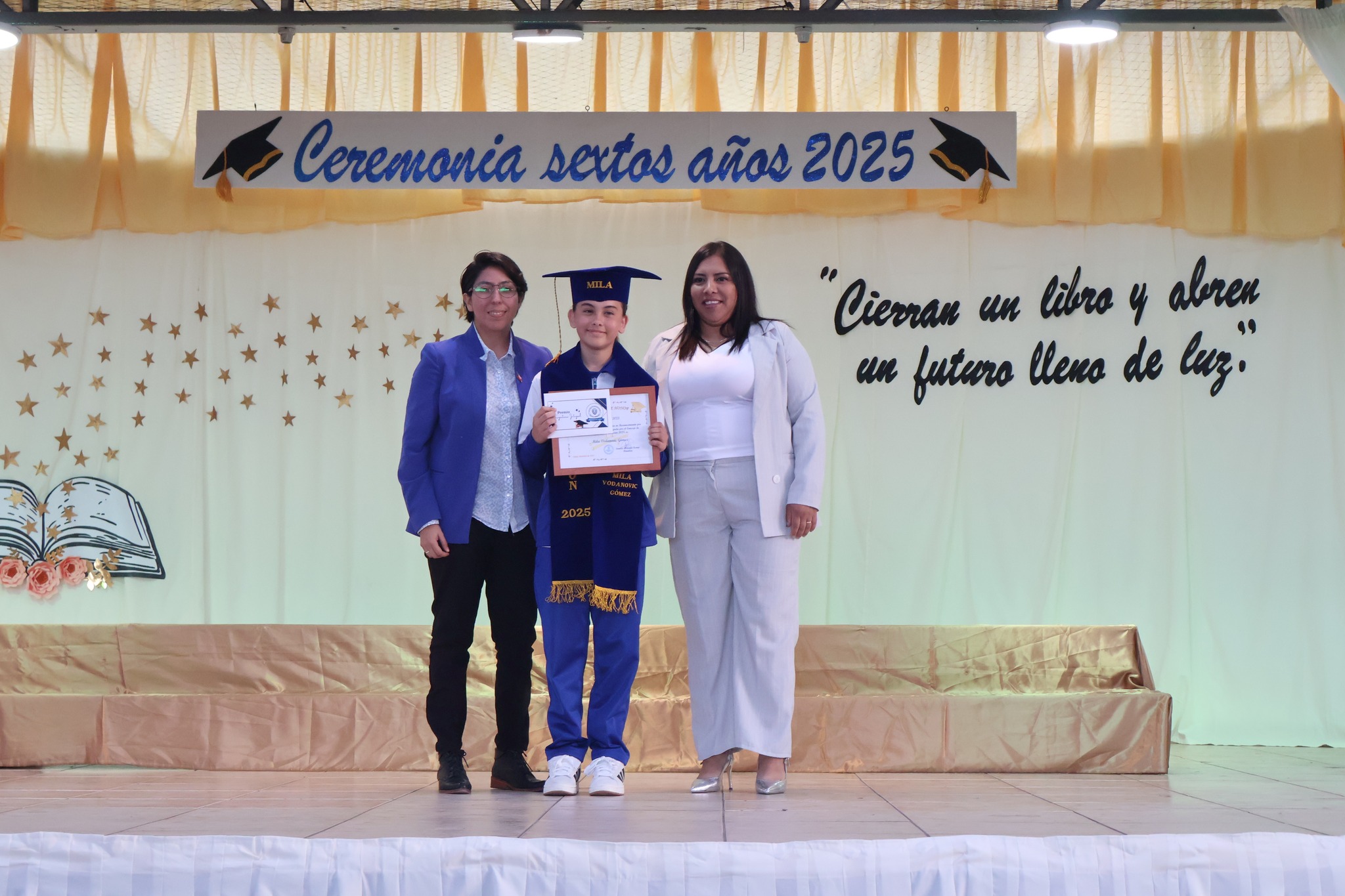 Estudiante posa con certificado en escenario durante la ceremonia de sextos años 2025.