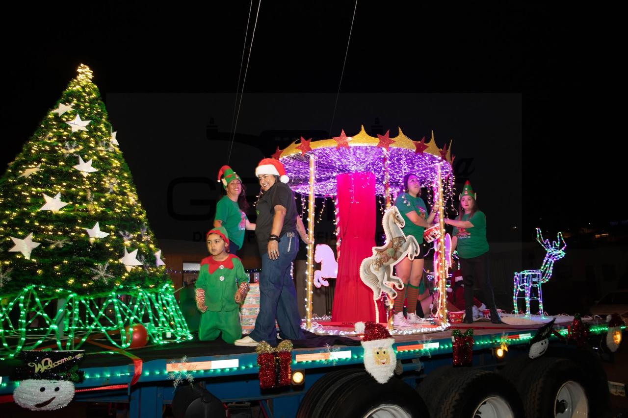Carro alegórico con gran árbol de Navidad y carrusel iluminado, con asistentes vestidos de duendes, en Taltal.