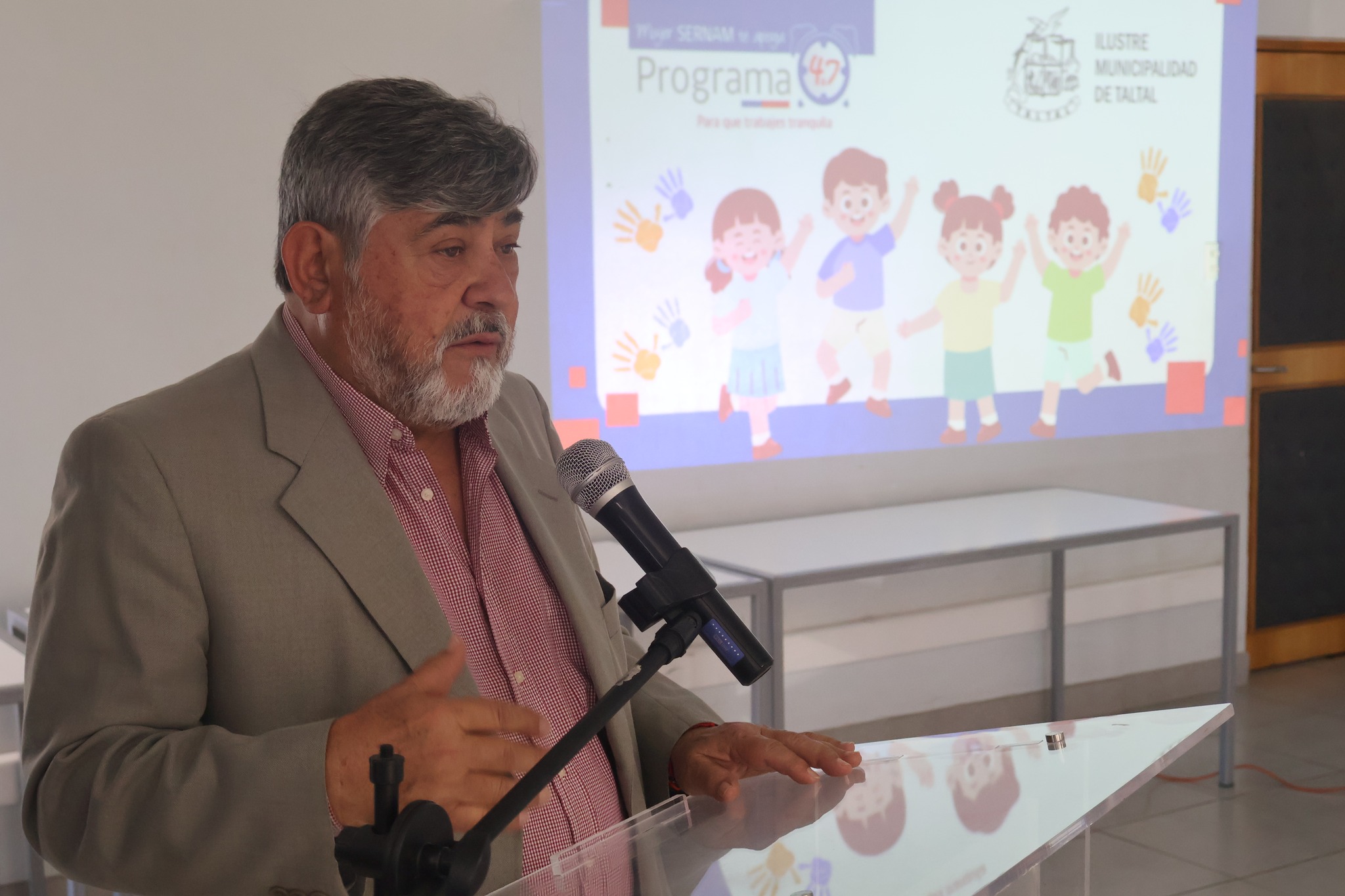 Autoridad municipal interviene en la ceremonia de cierre del Programa 4 a 7 2025 en Taltal, con presentación del programa al fondo.