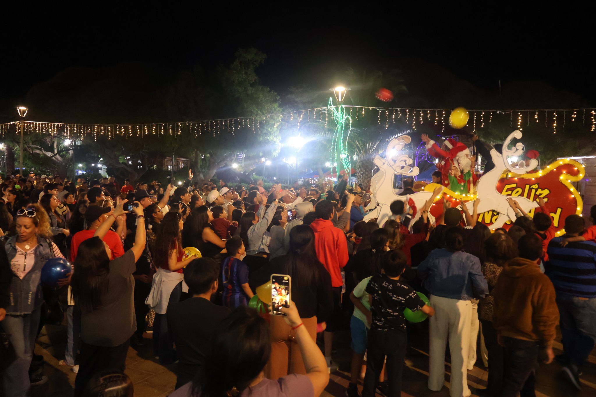 Familias reunidas en la plaza mientras se reparten dulces y sorpresas frente a letrero “Feliz Navidad” en Taltal.
