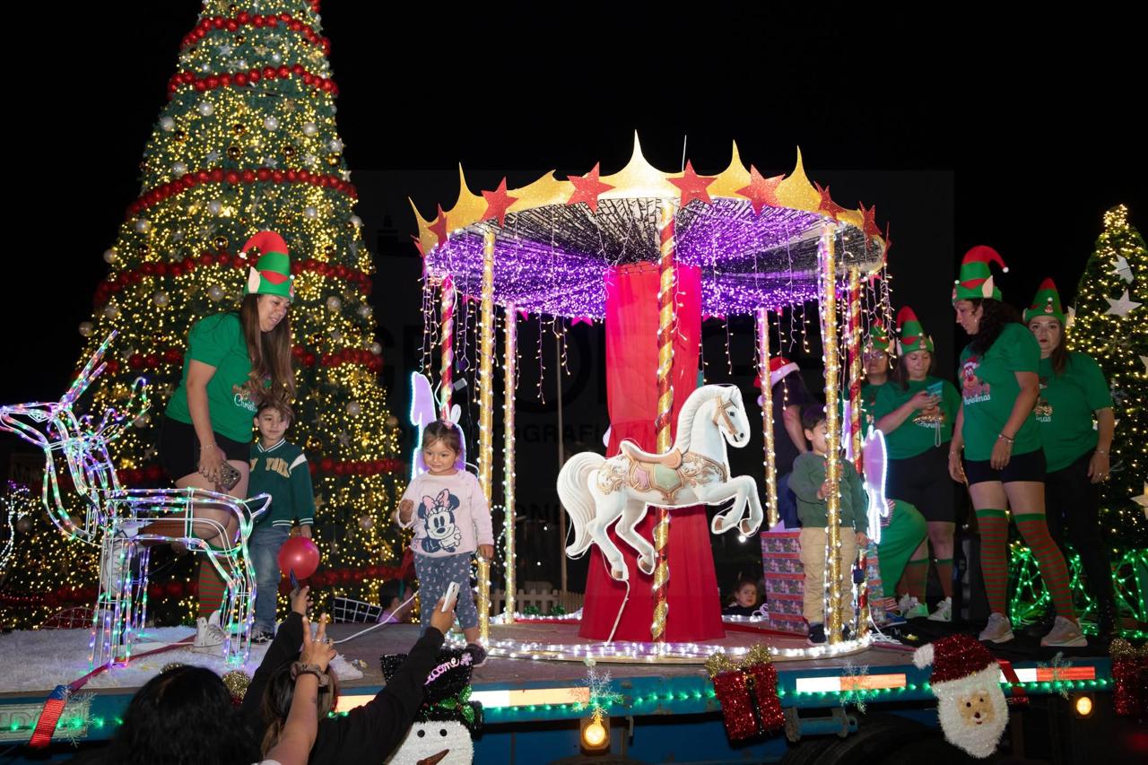 Niñas y niños junto a carro alegórico con carrusel iluminado y decoración navideña durante la Caravana Navideña en Taltal.