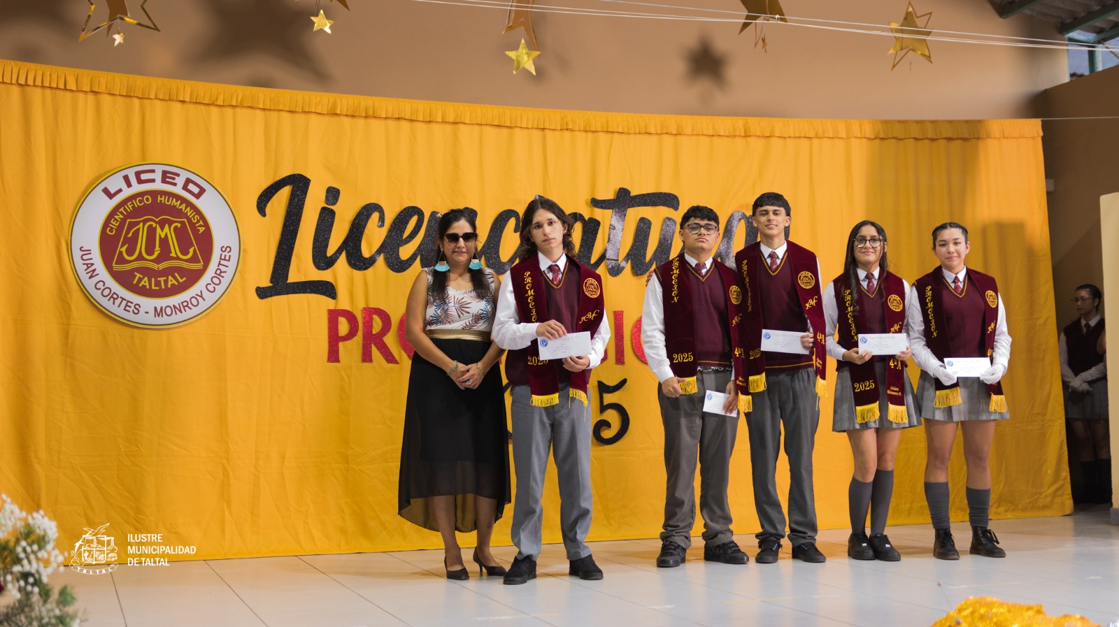 Estudiantes del 4° Año A posando con sus licencias de enseñanza media en el escenario.