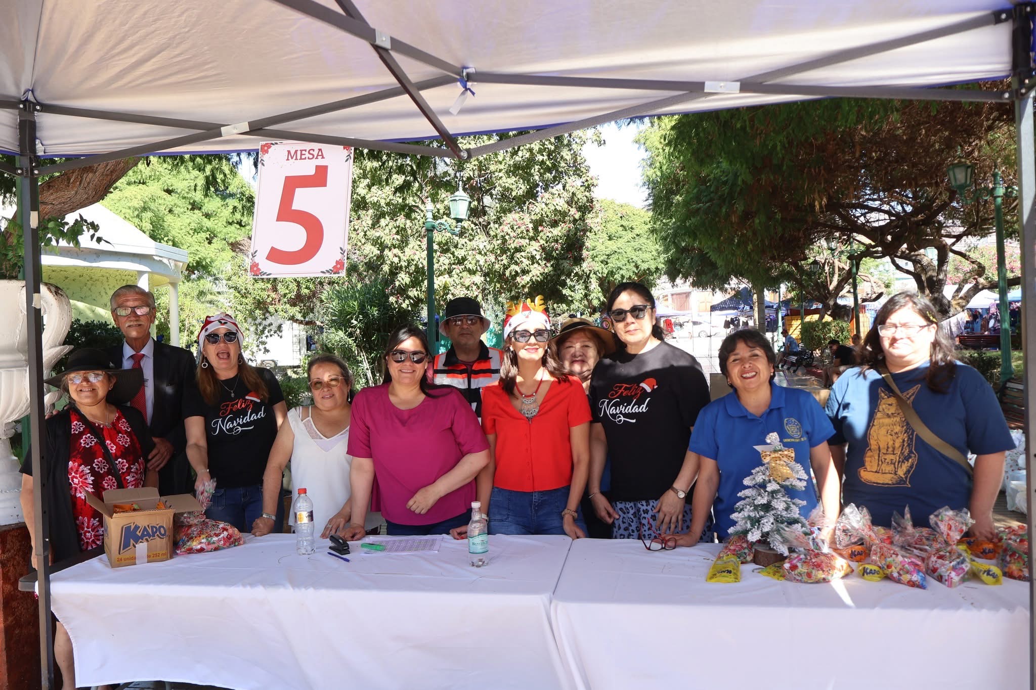 Equipo organizador posa en stand de entrega de regalos durante Navidad en familia en Plaza Prat de Taltal.