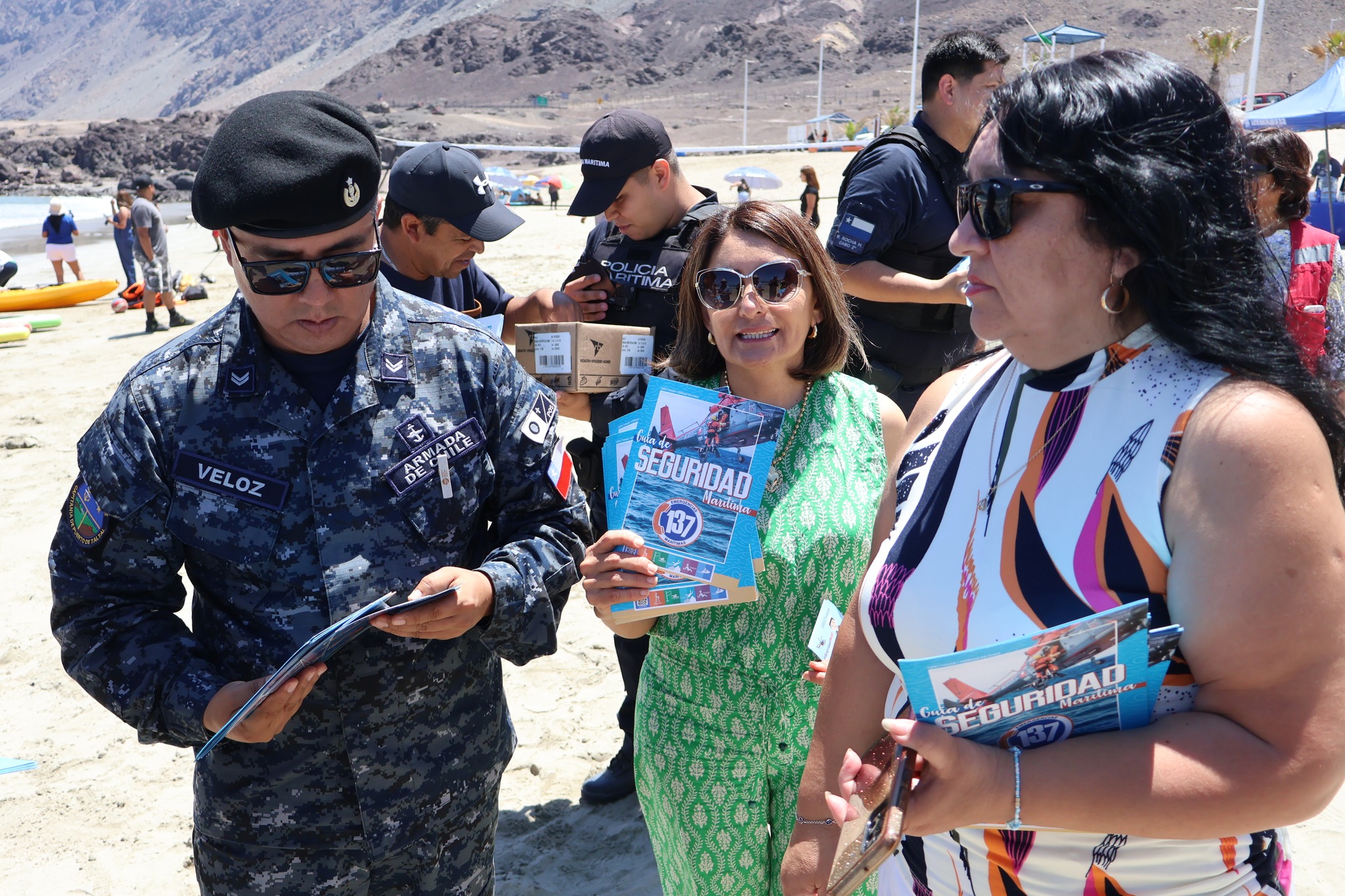 Autoridades y personal de la Armada entregando folletería de seguridad marítima a visitantes de la playa.