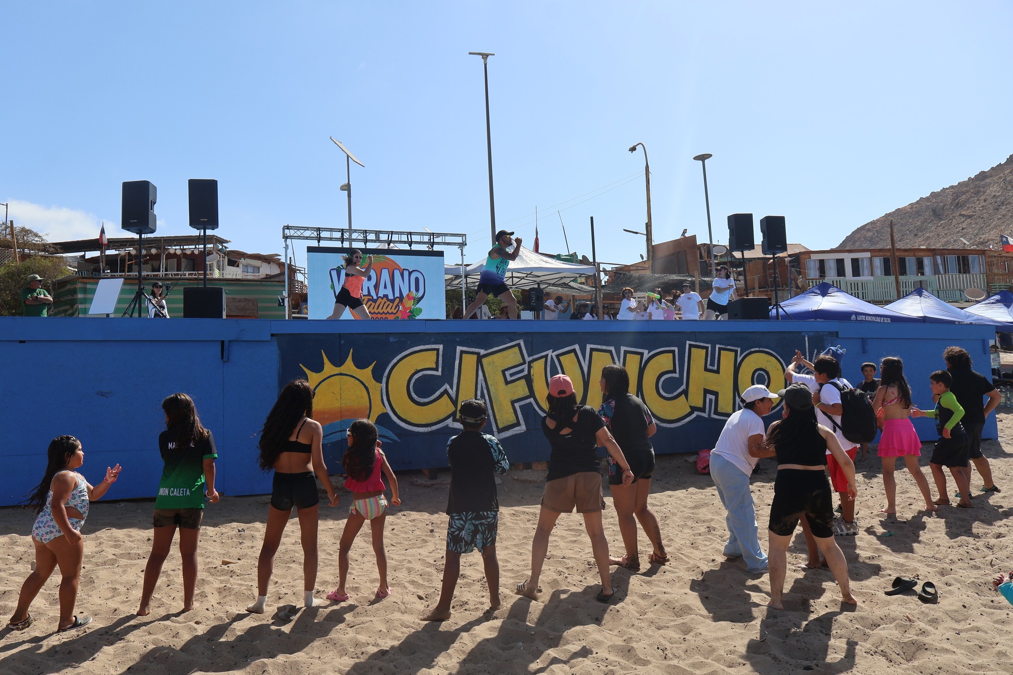 Niños y adultos participando en clases de baile frente al mural "Cifuncho" en el borde costero.