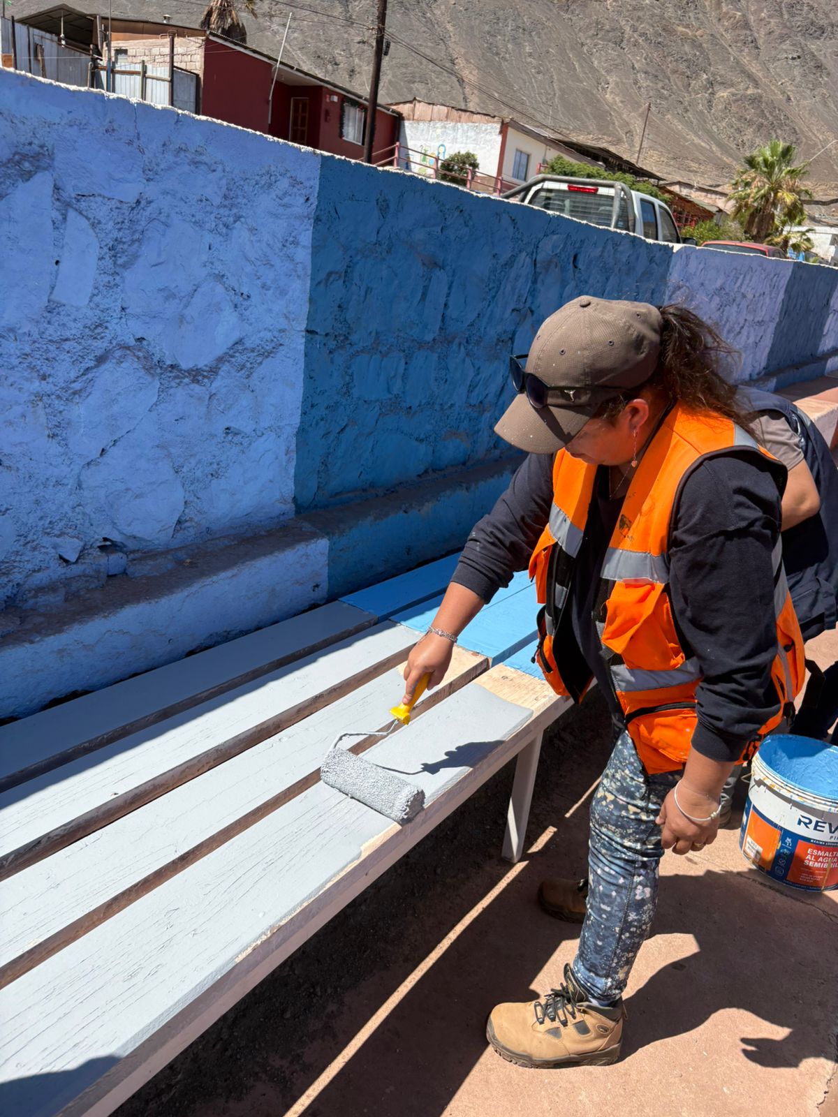 Trabajadora municipal aplicando pintura gris y azul en las bancas de madera de las graderías del estadio.