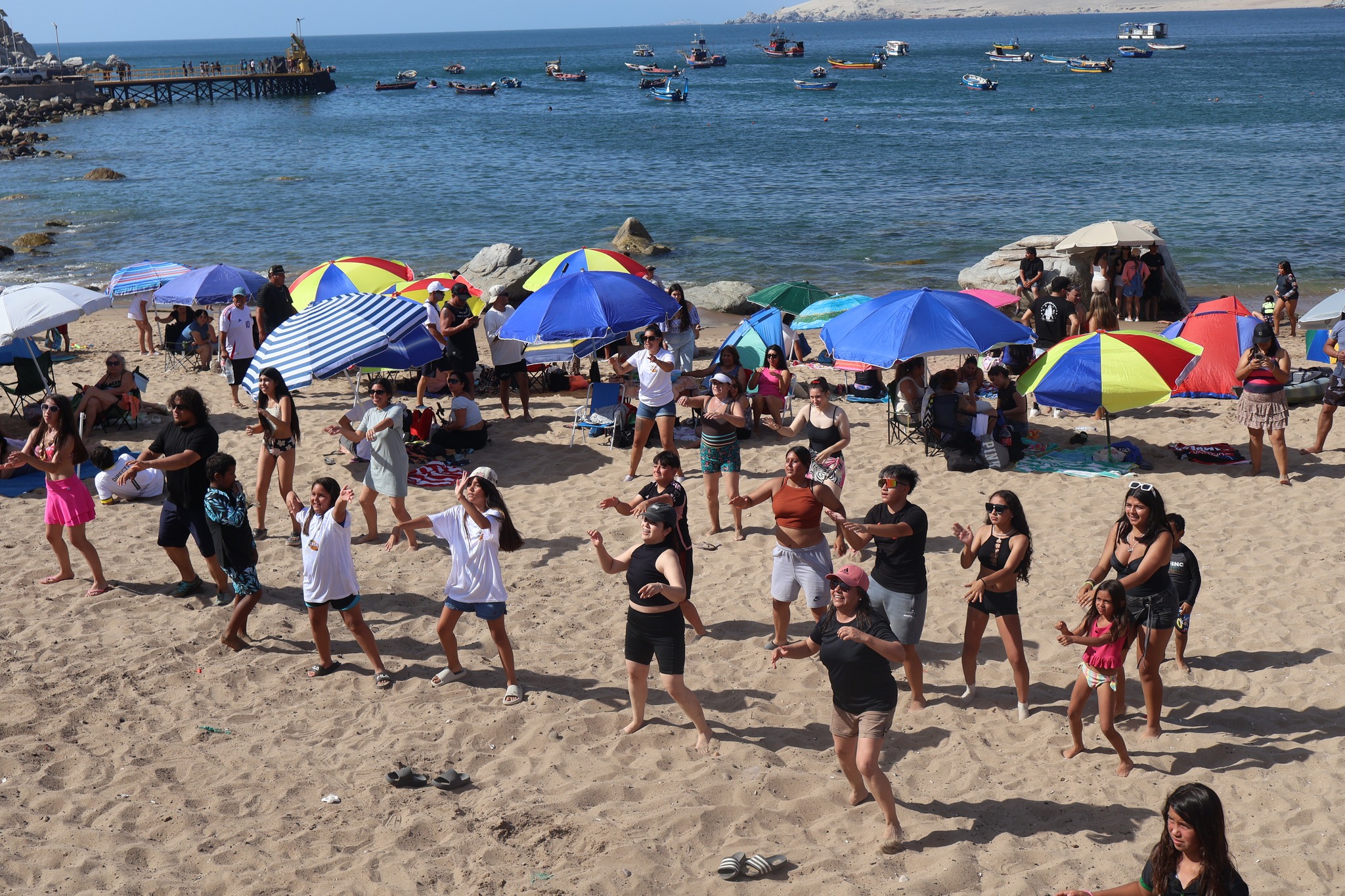 Grupo de jóvenes y niños participando en clases de baile entretenido en la orilla de la playa.