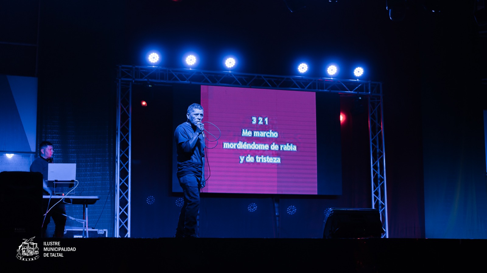 Participante masculino cantando frente a pantalla de letras en evento municipal de Taltal.