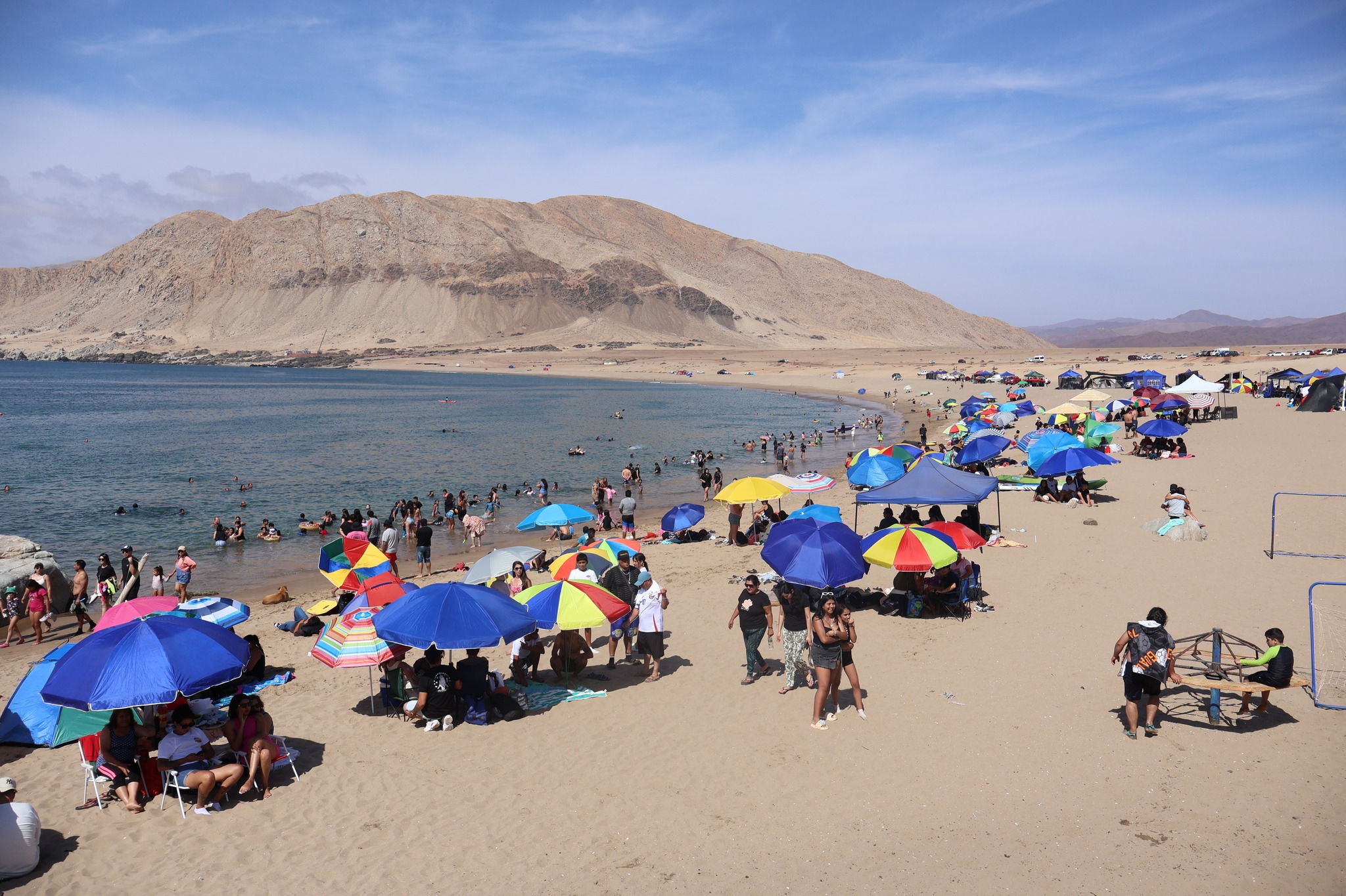 Vista panorámica de sombrillas multicolores y bañistas en la caleta durante la jornada festiva.
