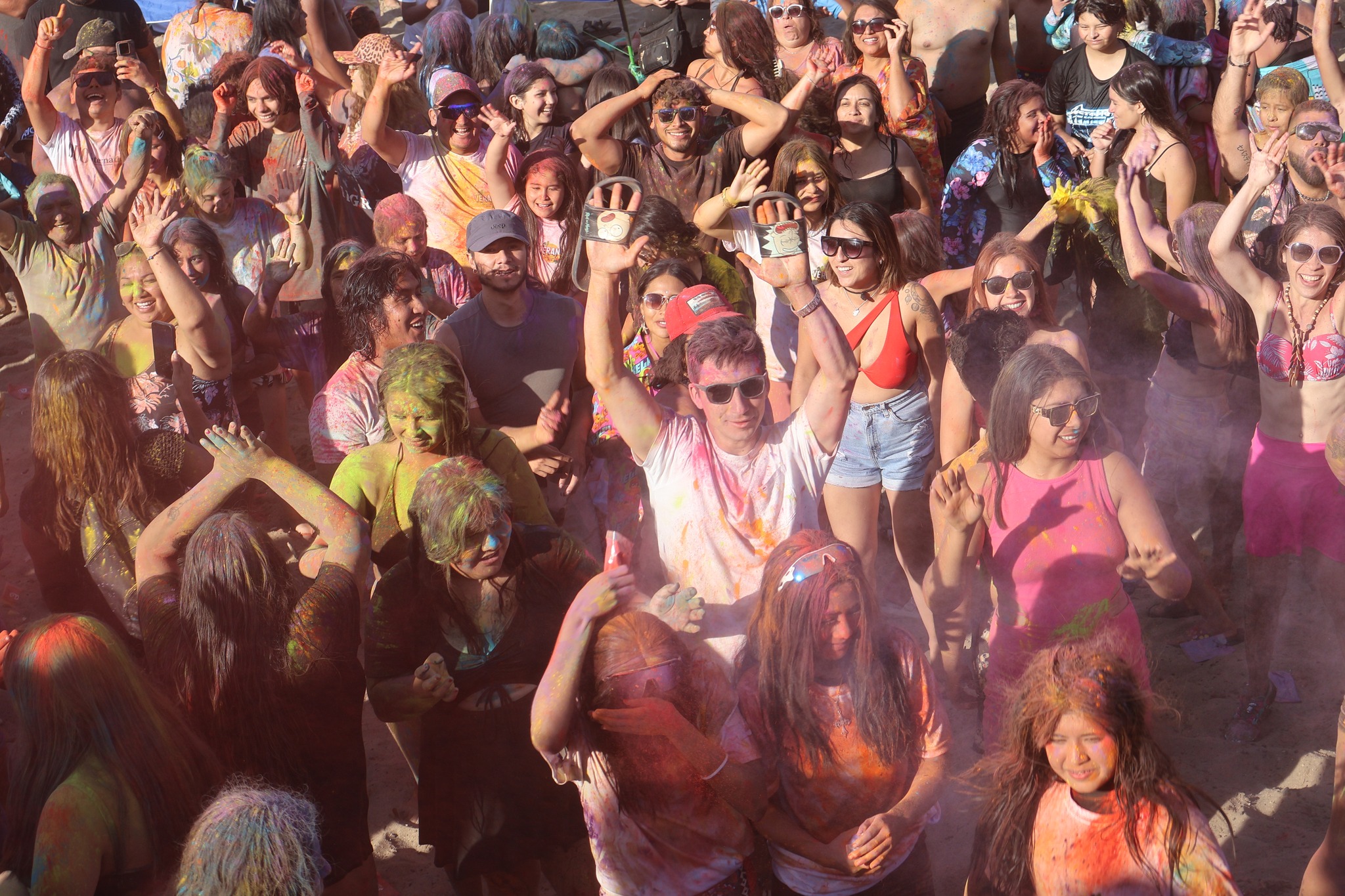 Multitud de jóvenes y adultos cubiertos de polvos de colores celebrando en la caleta de Cifuncho.