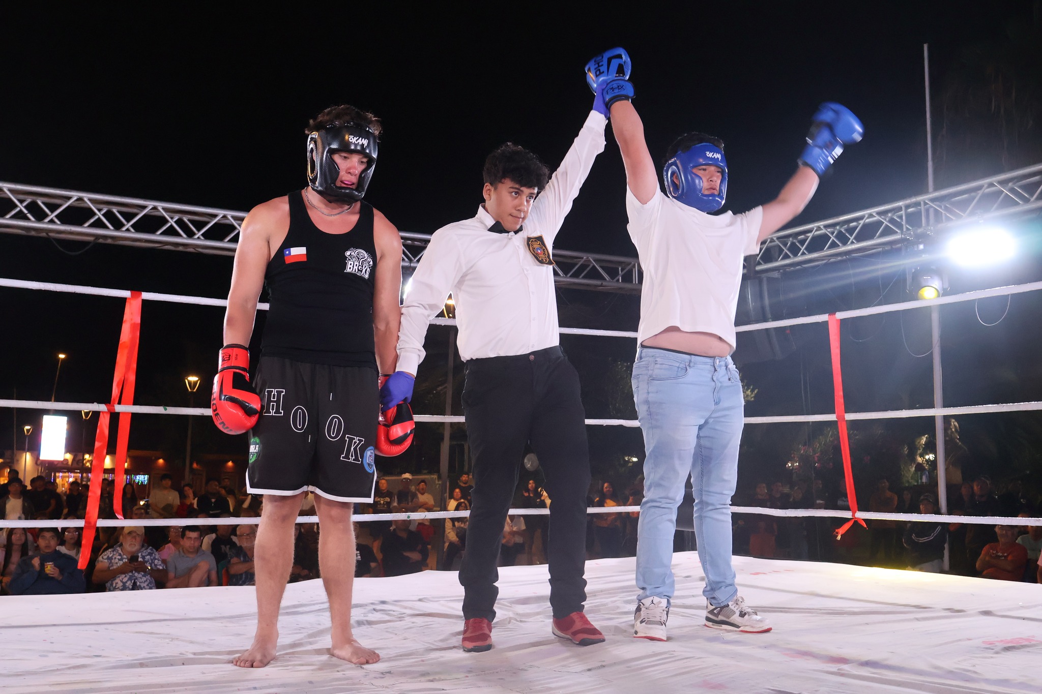 Un joven boxeador con cabezal y guantes azules celebrando su victoria en el ring ante la mirada de la comunidad taltalina.