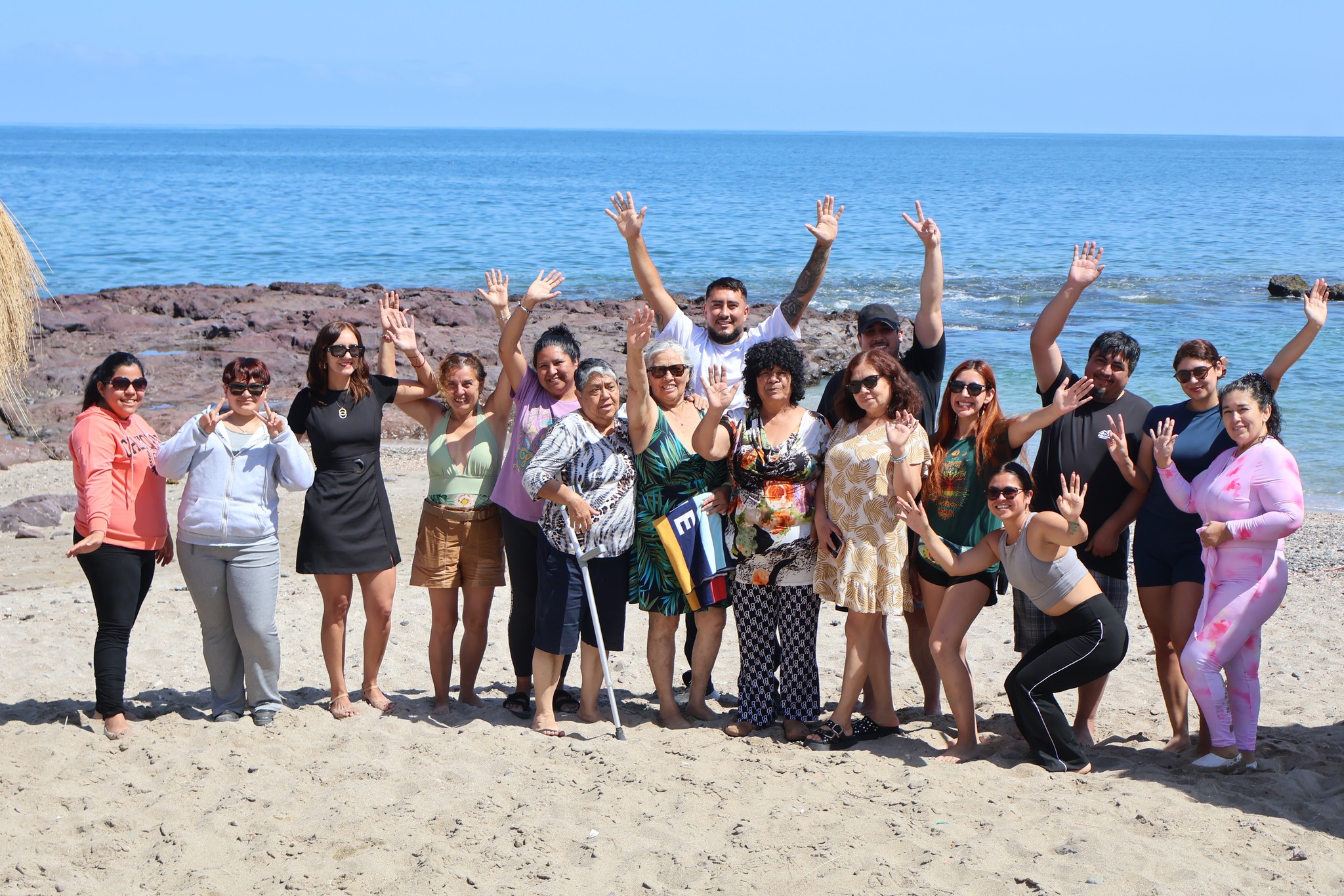 Grupo de personas cuidadoras saludando en la playa Poza La Tortuga tras jornada de bienestar.